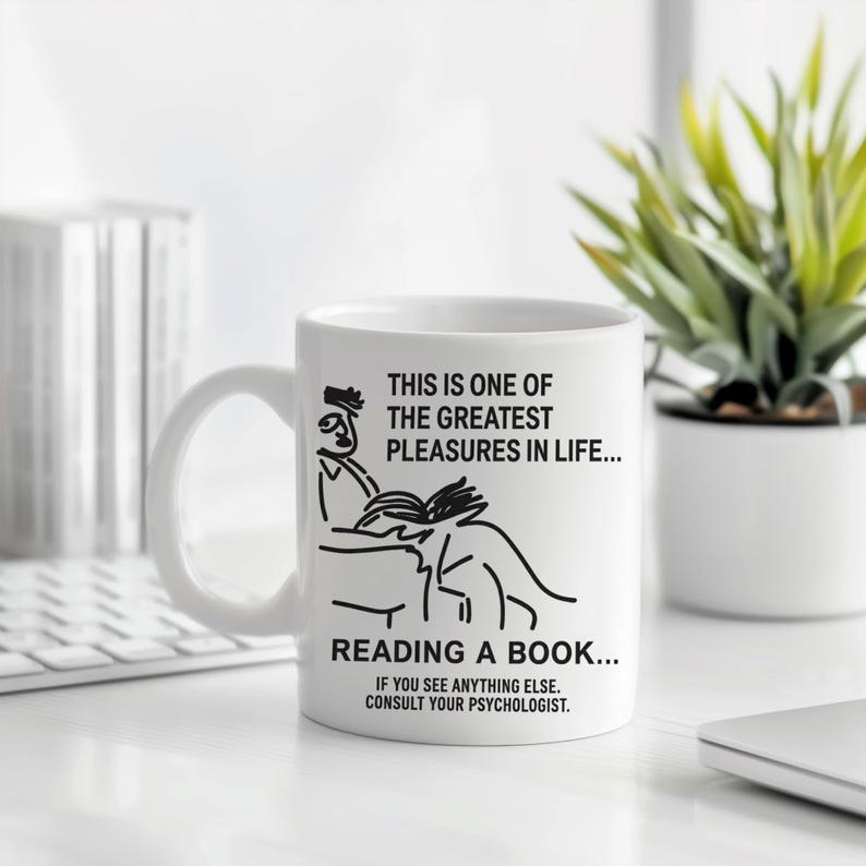 May include: White ceramic mug with a black line drawing of a person reading a book. The mug has text that reads, "THIS IS ONE OF THE GREATEST PLEASURES IN LIFE... READING A BOOK... IF YOU SEE ANYTHING ELSE. CONSULT YOUR PSYCHOLOGIST."