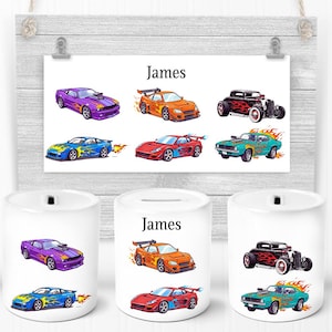 May include: White ceramic money banks featuring illustrations of colourful cars and the name "James". The cars are depicted in purple, orange, red, blue, and green, with flame details. A matching poster is displayed above.