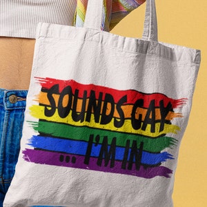 May include: A white canvas tote bag with rainbow stripes and the text "Sounds Gay I'm In" in black.