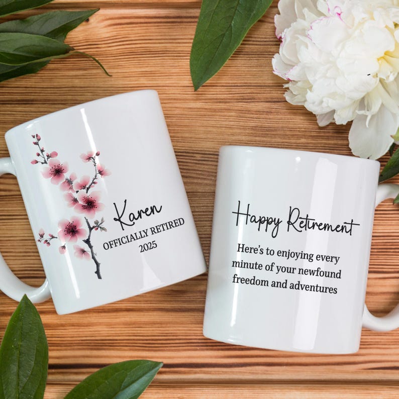 May include: Two white ceramic mugs. One mug has a floral design with pink blossoms and the name "Karen" with "OFFICIALLY RETIRED 2025". The other mug says "Happy Retirement" with a message about enjoying freedom.