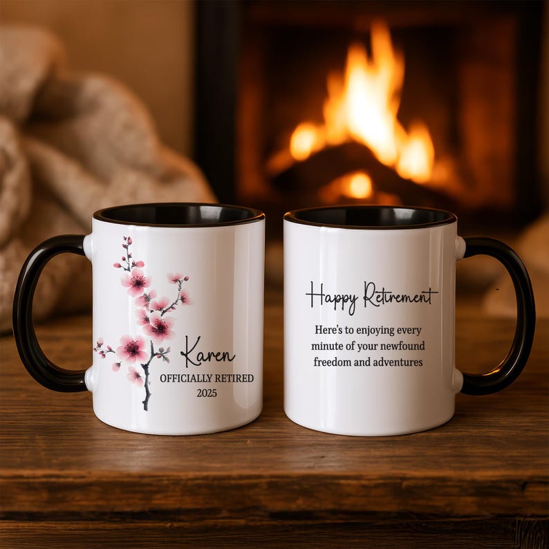 May include: Two white ceramic mugs with black handles and rims. One mug features pink cherry blossoms and the name "Karen" with "OFFICIALLY RETIRED 2025." The other mug says "Happy Retirement" with a message.