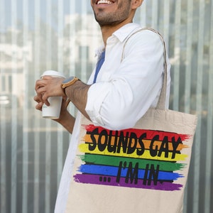 May include: A white canvas tote bag with rainbow stripes and the text "Sounds Gay I'm In".