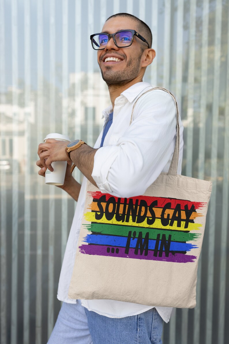 May include: A white canvas tote bag with rainbow stripes and the text "Sounds Gay I'm In".