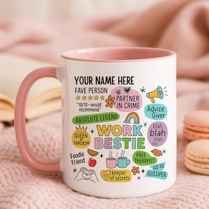 May include: White ceramic mug with a pink handle and rim, featuring colorful text and graphics. The mug says "YOUR NAME HERE" and "WORK BESTIE" with other phrases like "FAVE PERSON" and "FREE THERAPIST".