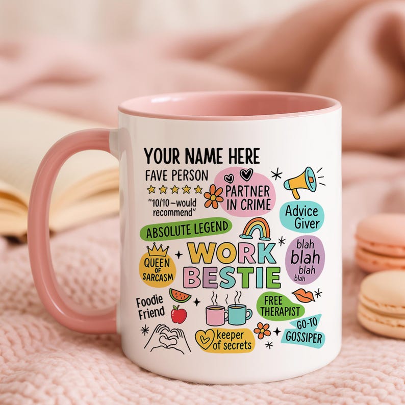 May include: White ceramic mug with a pink handle and rim, featuring colorful text and graphics. The mug says "YOUR NAME HERE" and "WORK BESTIE" with other phrases like "FAVE PERSON" and "FREE THERAPIST".