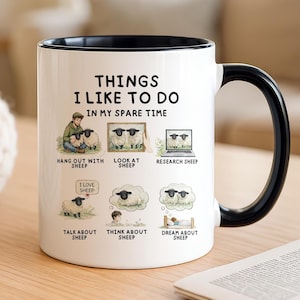 May include: A white ceramic mug with a black interior and handle, featuring the text "THINGS I LIKE TO DO IN MY SPARE TIME" and six illustrations of sheep-related activities including hanging out, looking at, researching, talking, thinking, and dreaming about sheep.