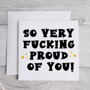 以下が含まれることがあります： 白いカードに黒い文字で「So very fucking proud of you!」と書かれており、単語「proud」の両側に金色の星が描かれています。