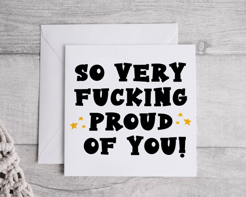 以下が含まれることがあります： 白いカードに黒い文字で「So very fucking proud of you!」と書かれており、単語「proud」の両側に金色の星が描かれています。
