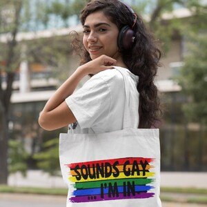 May include: A white tote bag with a rainbow stripe design and the text "Sounds Gay I'm In".