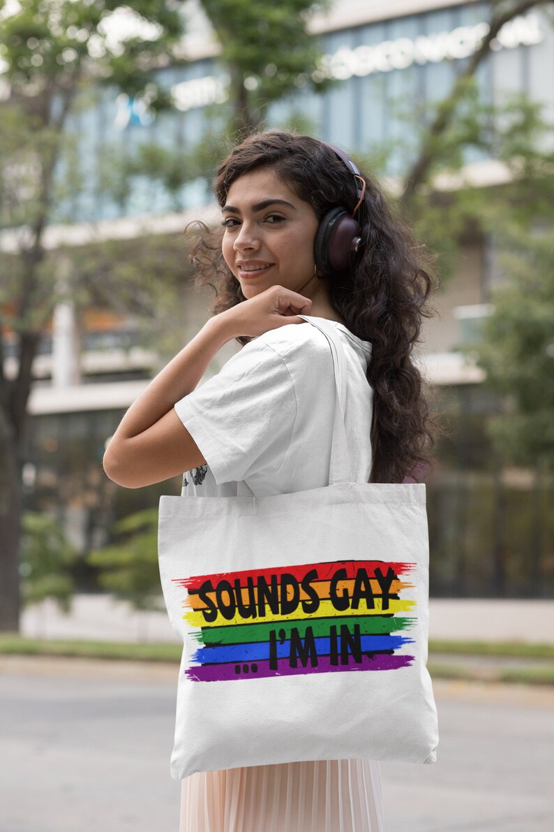 May include: A white tote bag with a rainbow stripe design and the text "Sounds Gay I'm In".