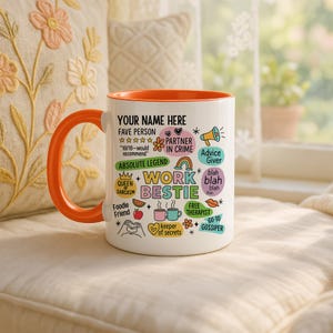 May include: White ceramic mug with an orange interior and handle. The mug features the text "YOUR NAME HERE" and various phrases like "Work Bestie," "Partner in Crime," and "Free Therapist." Decorative elements include hearts, stars, and a rainbow.
