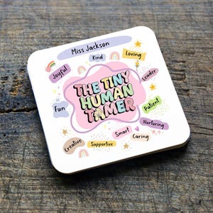 Peut inclure: Un dessous de verre carré blanc aux coins arrondis. Le dessous de verre présente le texte "THE TINY HUMAN TAMER" dans un design de nuage rose. Autour du texte se trouvent des mots comme "Joyful", "Kind", "Loving" et "Creative".