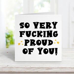 以下が含まれることがあります： 「So very fucking proud of you!」という黒い文字が書かれた白いカード。proudの両側に金色の星が2つある。