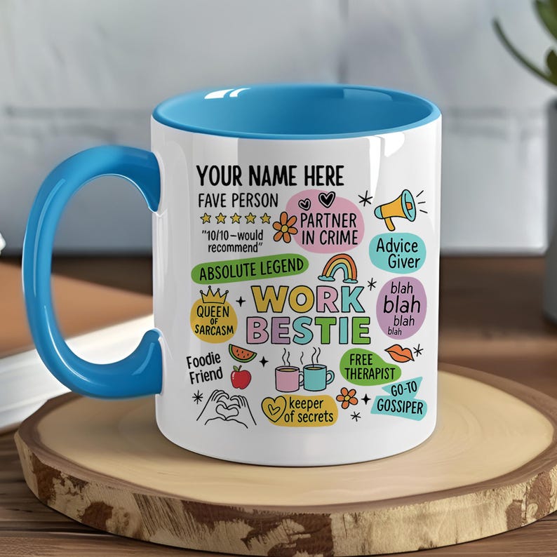 May include: A white ceramic mug with a blue interior and handle. The mug features the text "WORK BESTIE" in colorful letters, along with various doodles and phrases like "FAVE PERSON" and "ABSOLUTE LEGEND".