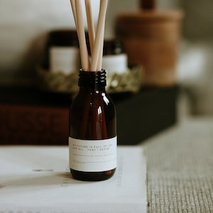 May include: A brown glass bottle with a white label that reads "My future is full of joy and all that I desire". The bottle has wooden sticks sticking out of the top. The bottle is sitting on a white book.