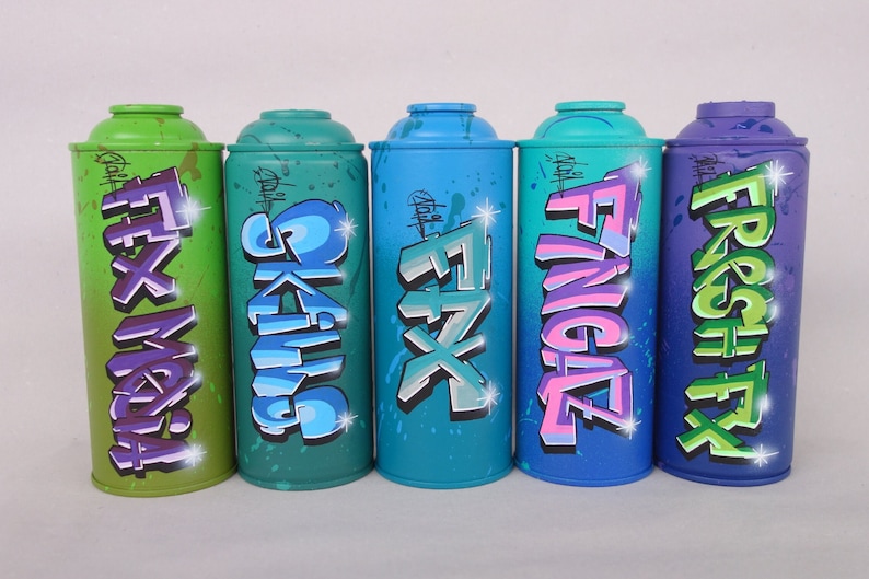 May include: Five spray paint cans with different colors and graffiti designs. The cans are labeled "FX Mafia", "Skulls", "FX", "Fingaz", and "Fresh FX".