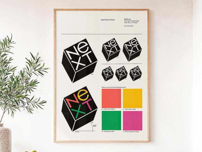 May include: A framed specification sheet featuring the "NEXT" logo in a cube design. The logo appears in black and white, and in a colorful version. Color swatches are included. The frame is light brown.