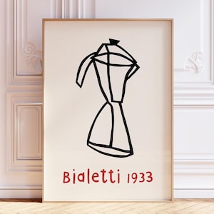 Op de afbeelding: Ingelijste kunstdruk met een minimalistische zwarte lijntekening van een Bialetti espressomaker. De tekst "Bialetti 1933" staat in het rood. Het kunstwerk staat tegen een crèmekleurige achtergrond.