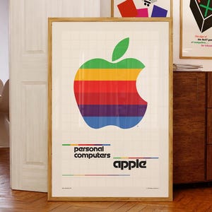 以下が含まれることがあります： 鮮やかな虹色のデザインの、象徴的なAppleロゴが特徴の額入りポスター。ポスターには、レトロなフォントで「personal computers」と「apple」という言葉が含まれています。このアートワークは、木製の床と白いドアのある部屋に展示されています。