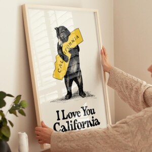 May include: A framed print featuring a black bear hugging a yellow outline of the state of California. The text "I Love You California" is printed below the bear.