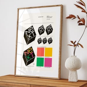 May include: A framed print featuring the word "NEXT" in a 3D cube design, repeated in various sizes and orientations. The print includes a color palette of red, yellow, green, and pink. The artwork is displayed on a wooden cabinet.