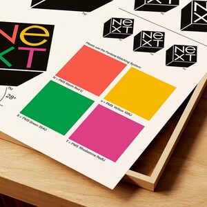 May include: A print featuring the "NEXT" logo in a 3D cube design, with color swatches and text. The logo uses red, green, yellow, and pink. The text includes "Please use the Pantone Matching System:" and color names.