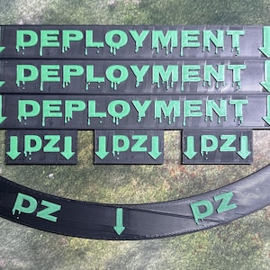 May include: Three black and green rectangular signs with the word "DEPLOYMENT" printed in green letters with dripping green paint. Three smaller black and green rectangular signs with the word "IDZI" printed in green letters with dripping green paint. A black curved sign with the word "DZ" printed in green letters.