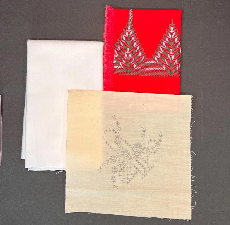May include: An assortment of fabric pieces, including a folded white cloth, a red square with embroidered green and white designs, and a beige square with a floral embroidery pattern. The edges of the red and beige squares are unfinished.