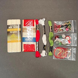May include: A collection of sewing supplies including white hem facing, red and white thread spools, green thread spools, red cording, and various beads and buttons in small plastic bags. The text "FLEXI-Lace HEM FACING" is visible.