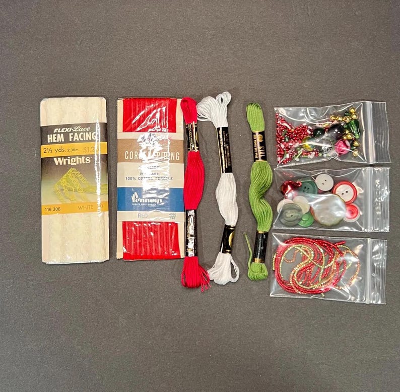 May include: A collection of sewing supplies including white hem facing, red and white thread spools, green thread spools, red cording, and various beads and buttons in small plastic bags. The text "FLEXI-Lace HEM FACING" is visible.