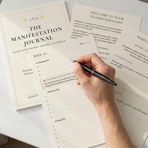 Könnte beinhalten: Ein cremefarbenes Journal mit dem Titel "The Manifestation Journal" mit dem Text "Align Your Energy, Rewire Your Brain". Eine Hand, die einen schwarzen Stift hält, schreibt auf eine Seite mit dem Text "Day 12". Zusätzliche Seiten enthalten "Welcome to Your Transformation" und "Weekly Reflection".