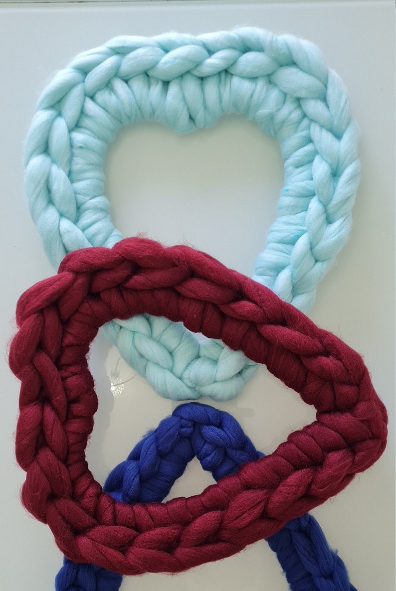 Puede incluir: Tres coronas de coraz&oacute;n de lana tejidas en colores azul, rojo y azul oscuro. Las coronas est&aacute;n apiladas con la corona azul en la parte superior, la corona roja en el medio y la corona azul oscuro en la parte inferior.