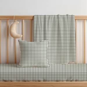 May include: A sage green and white gingham patterned square throw cushion, a matching rectangular blanket draped over a wooden cot rail, and a crescent moon-shaped plush toy hanging from the top rail of the wooden cot structure.