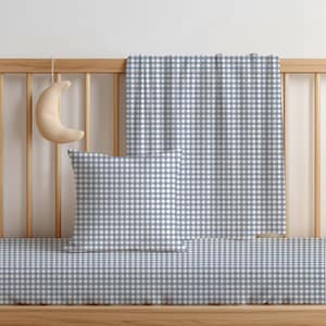Könnte beinhalten: Ein quadratisches Dekokissen und eine rechteckige Decke mit blau-weißem Vichy-Karomuster. Ein kleines, halbmondförmiges Plüschobjekt hängt am hölzernen Gitterbettgeländer, das sich hinter dem Kissen und der Decke befindet.