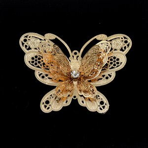 May include: Gold metal butterfly with a clear rhinestone in the center. The butterfly has a delicate, intricate design.