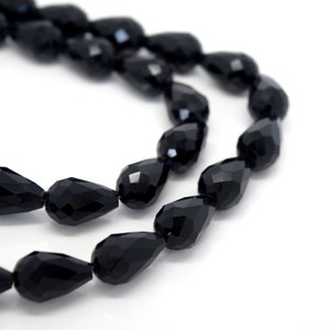 May include: A strand of black faceted teardrop beads. The beads are strung on a clear thread and are arranged in a loose, flowing pattern.