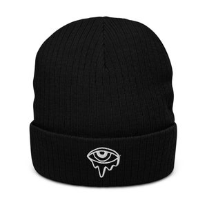 May include: Black knitted beanie with a white embroidered eye design that appears to be dripping.