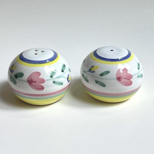 May include: A pair of spherical ceramic salt and pepper shakers featuring a white base with hand-painted floral motifs in pink and green, accented by horizontal bands of blue, yellow, and pink encircling the top and bottom of each piece.