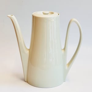 May include: Cream-colored ceramic coffee pot with a tall, slender body and a curved handle. The pot has a long, elegant spout and a matching lid with a small knob. The design is minimalist and modern, suitable for serving coffee or tea.