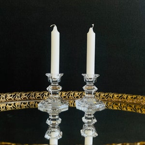 May include: Two white candles on clear glass candle holders, sitting on a gold mirrored tray.