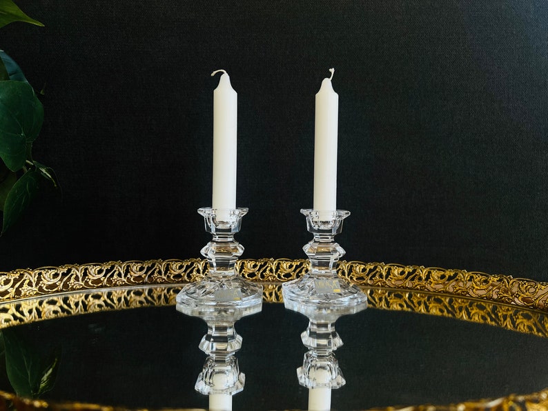 May include: Two white candles on clear glass candle holders, sitting on a gold mirrored tray.