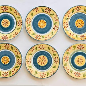 May include: Six ceramic plates with a floral design. Each plate features a yellow rim with red and orange flowers and green leaves. The center has a blue ring with a yellow and orange floral pattern.