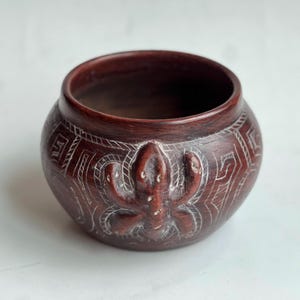 May include: A handcrafted, dark brown ceramic bowl with a carved octopus design. The bowl features white etched geometric patterns and a smooth, rounded shape. This decorative piece is suitable for home decor.