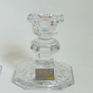 May include: A clear glass candle holder with a cut crystal design. The base of the holder has a gold label that reads "Mikasa Crystal of Japan".