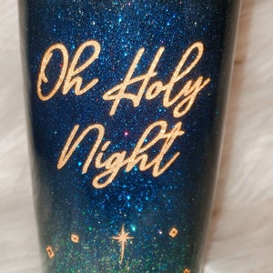 May include: A blue and green glitter tumbler with gold lettering that reads "Oh Holy Night". The tumbler features a silhouette of the nativity scene with a star above.