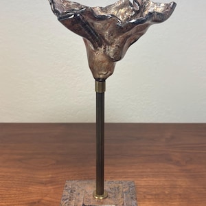 Peut inclure: Sculpture florale abstraite avec une finition métallique bronze et or. La fleur texturée repose sur une tige en métal foncé et striée, avec une base carrée à motifs superposés. Un objet décoratif unique pour la maison.