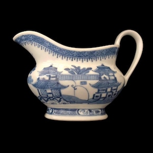 Può includere: Una salsiera in porcellana bianca e blu con manico e beccuccio. La barca presenta un design paesaggistico blu di ispirazione asiatica. Il bordo e la base hanno motivi blu decorativi. Un pezzo classico per servire salse.