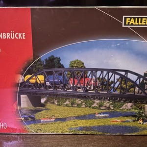 May include: A model railway set box showing an arched bridge. The box is red and brown with the text "Bogenbrücke" and "Arched Bridge". The image depicts a black bridge with a train crossing over a river with small boats and miniature figures.