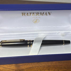 Pu&ograve; includere: Una penna Waterman nera con dettagli dorati &egrave; all'interno di un cofanetto blu. La scatola &egrave; foderata in raso bianco e presenta il marchio "WATERMAN PARIS" in lettere dorate. Un nastro bianco assicura la penna.