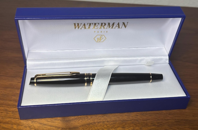 Pu&ograve; includere: Una penna Waterman nera con dettagli dorati &egrave; all'interno di un cofanetto blu. La scatola &egrave; foderata in raso bianco e presenta il marchio "WATERMAN PARIS" in lettere dorate. Un nastro bianco assicura la penna.